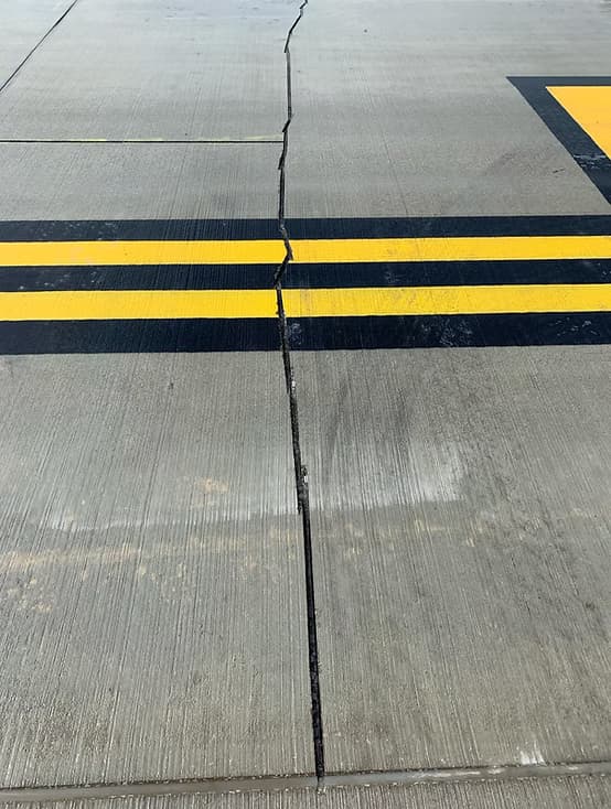 Repaired crack sealed with black filler running across a concrete slab and crossing double yellow line markings