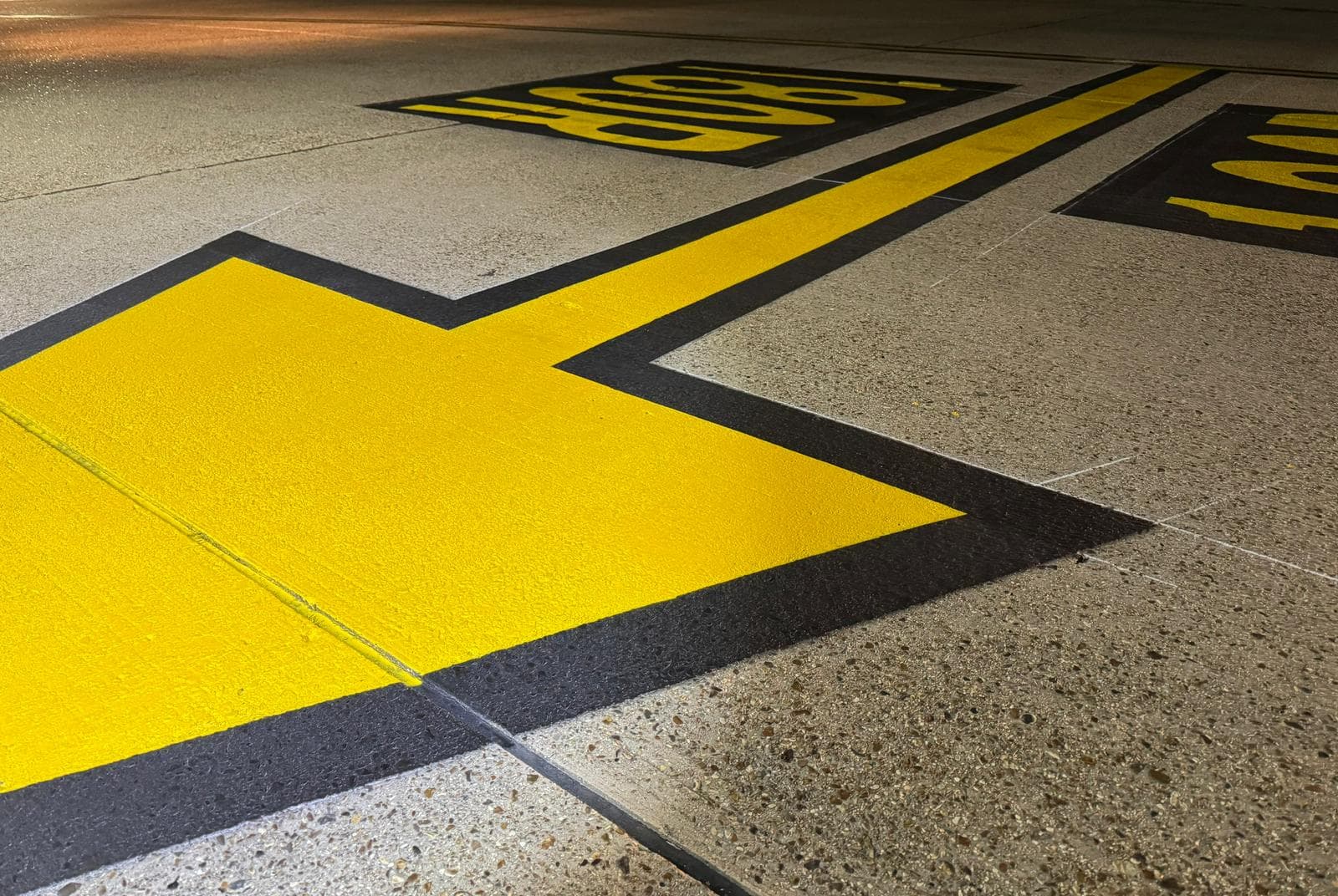 Close-up of freshly painted yellow airfield markings with black borders on a concrete surface