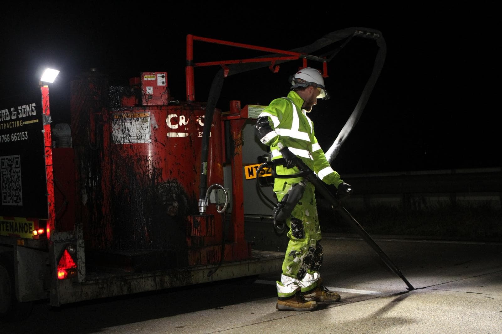 Worker in hi-vis applying hot joint sealant to a road at night with a lance beside a branded Shepherd and Sons machine