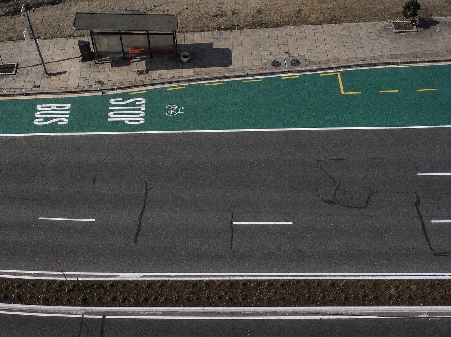 Aerial view of a green anti-skid bus lane with white BUS STOP and cycle markings beside a grey carriageway