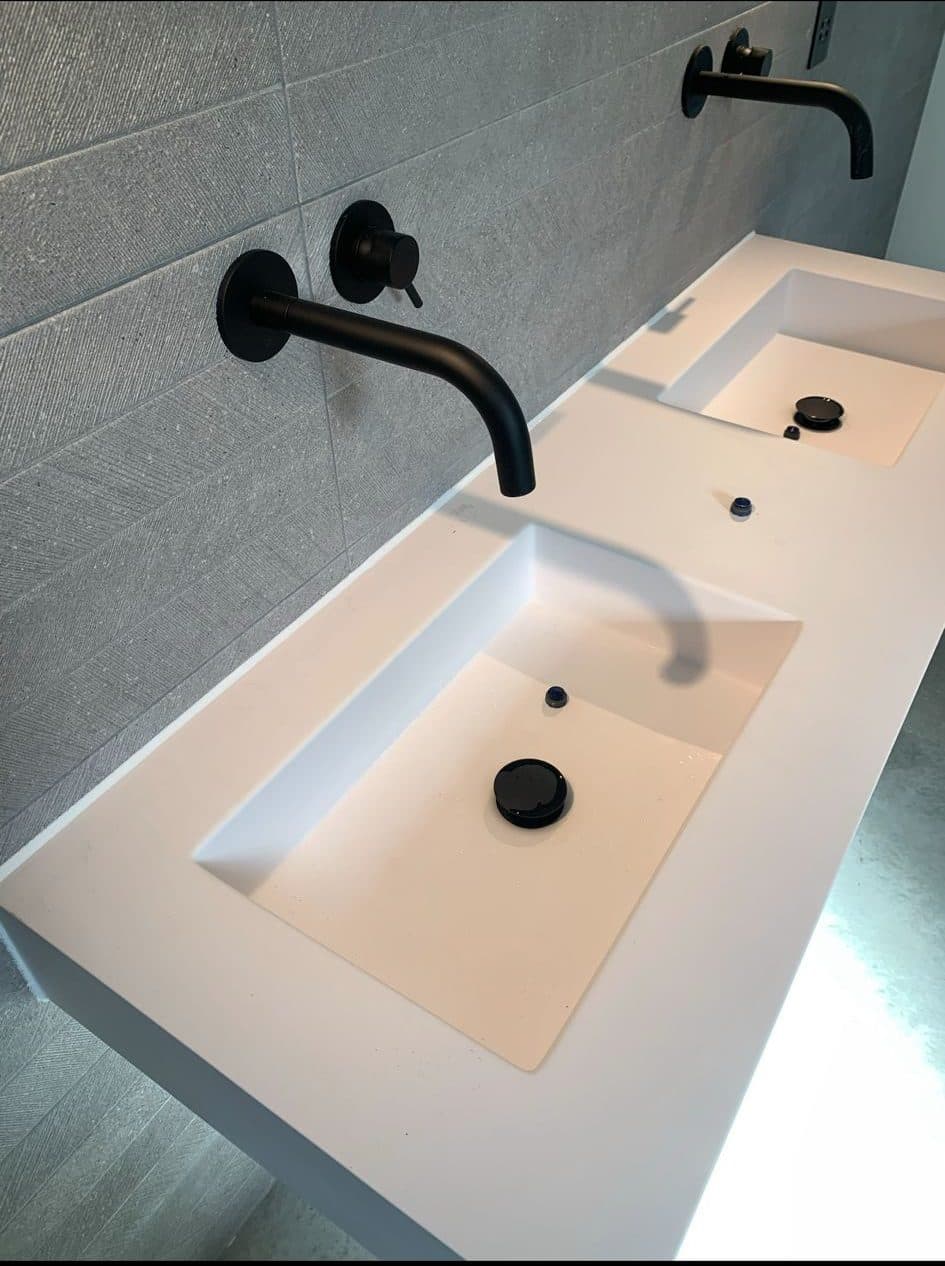 White twin countertop basin with matt black wall-mounted taps against grey tiling